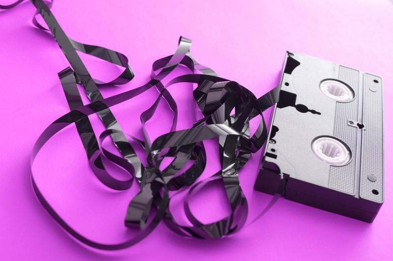 Free Stock Photo: Destroyed unwound VHS video tape and cassette on a bright magenta pink background in a concept of entertainment and technology